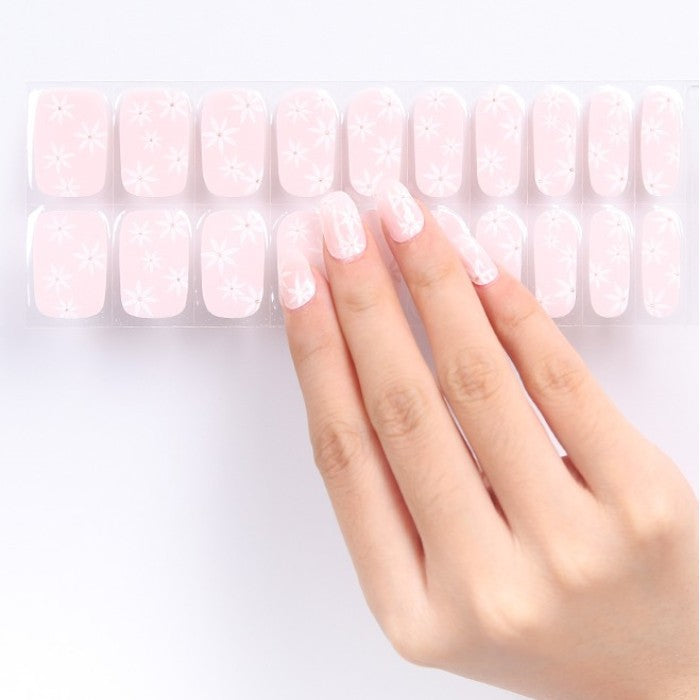 Sticker sheet presenting soft pink gel nail wraps with white daisy patterns in assorted sizes.